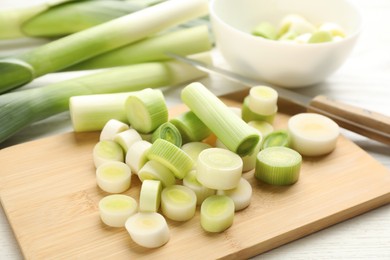 Photo of Fresh raw leek slices and knife on white wooden table, closeup