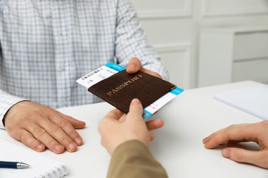 Photo of Manager giving passport and ticket to man at desk in travel agency office, closeup