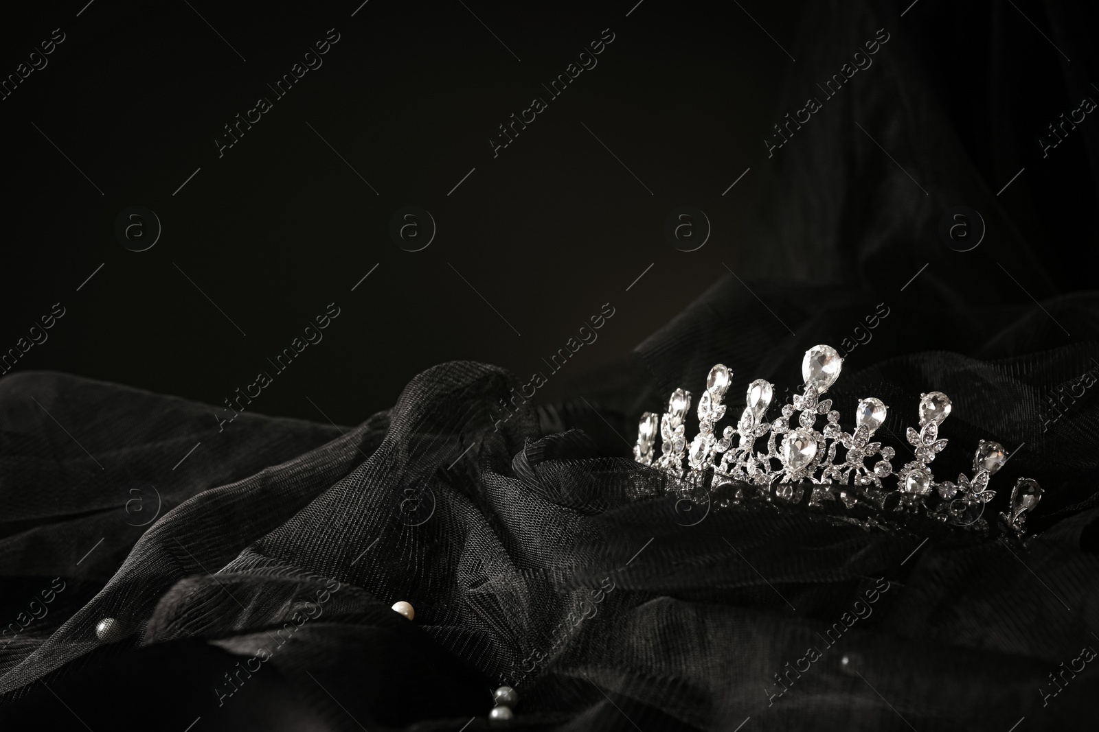 Photo of Beautiful silver tiara with diamonds on black cloth. Space for text
