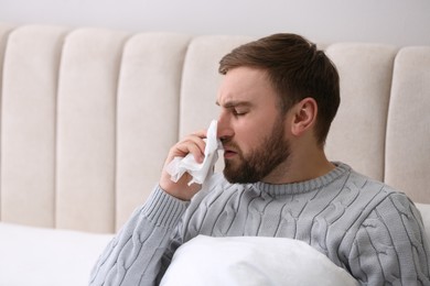 Photo of Young man suffering from runny nose in bed indoors