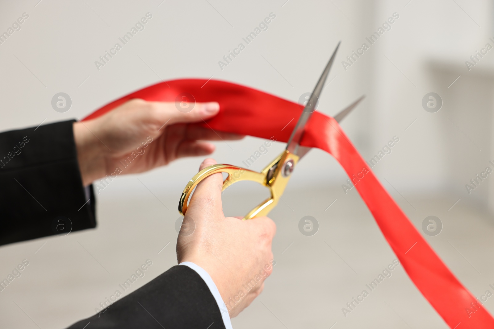 Photo of Woman cutting red ribbon with scissors indoors, closeup