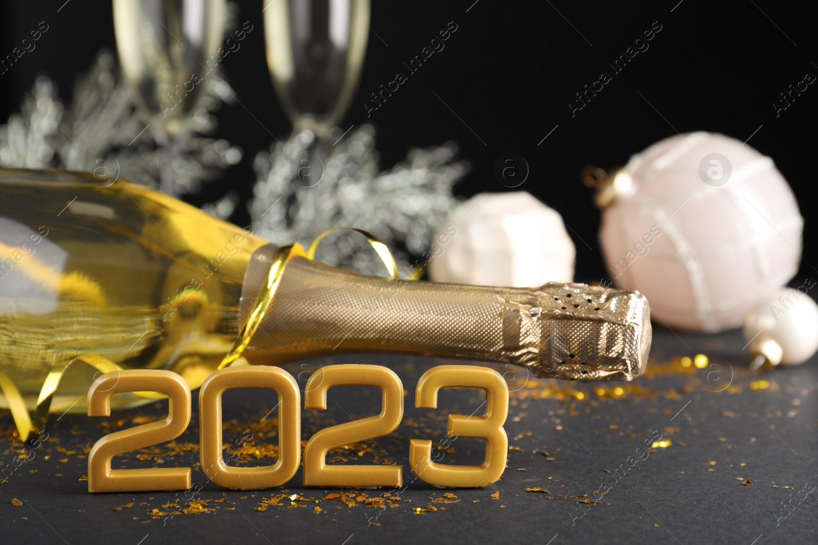 Photo of Happy New Year 2023! Bottle of sparkling wine and festive decor on table against black background