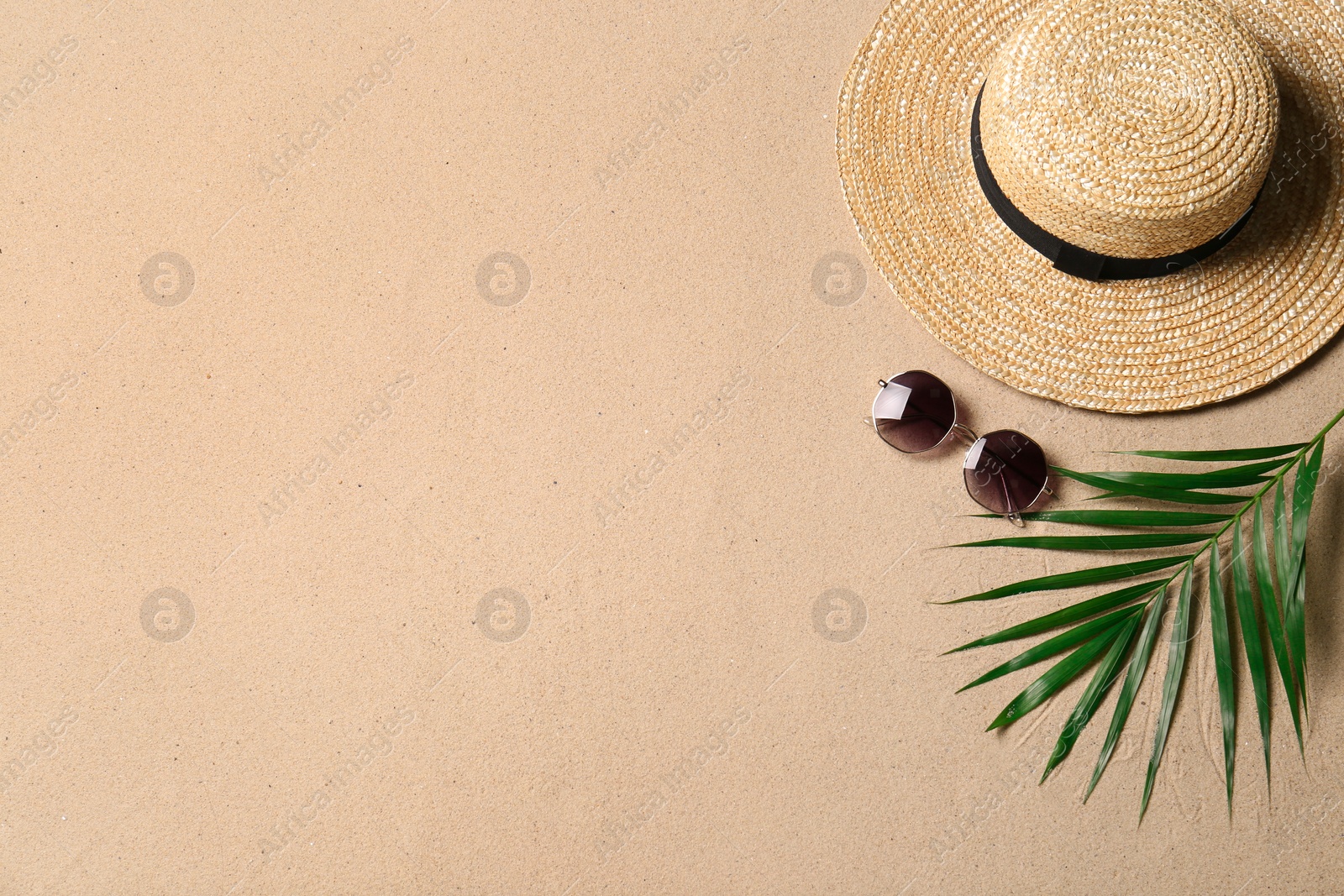 Photo of Straw hat, sunglasses, palm leaf and space for text on beach sand, flat lay. Summer vacation