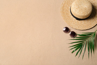 Photo of Straw hat, sunglasses, palm leaf and space for text on beach sand, flat lay. Summer vacation