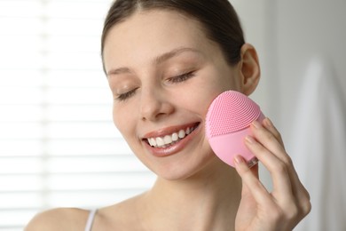 Photo of Washing face. Young woman with cleansing brush indoors, closeup