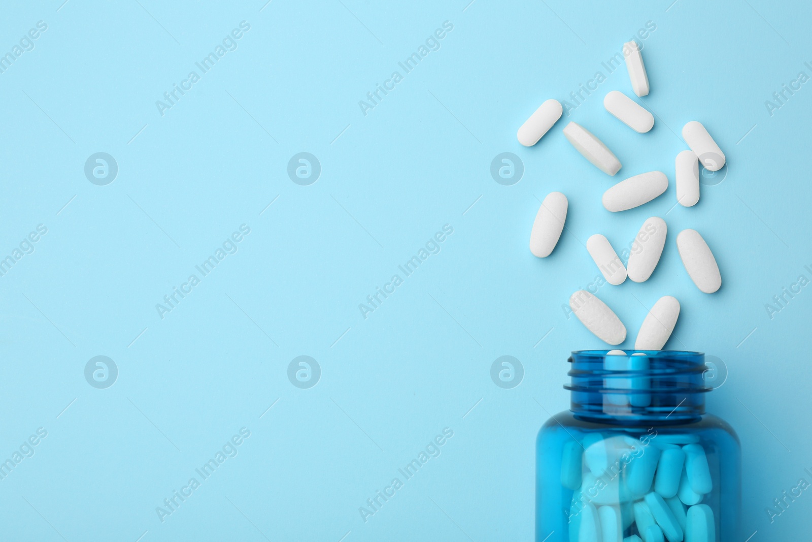 Photo of Vitamin pills and bottle on light blue background, top view. Space for text