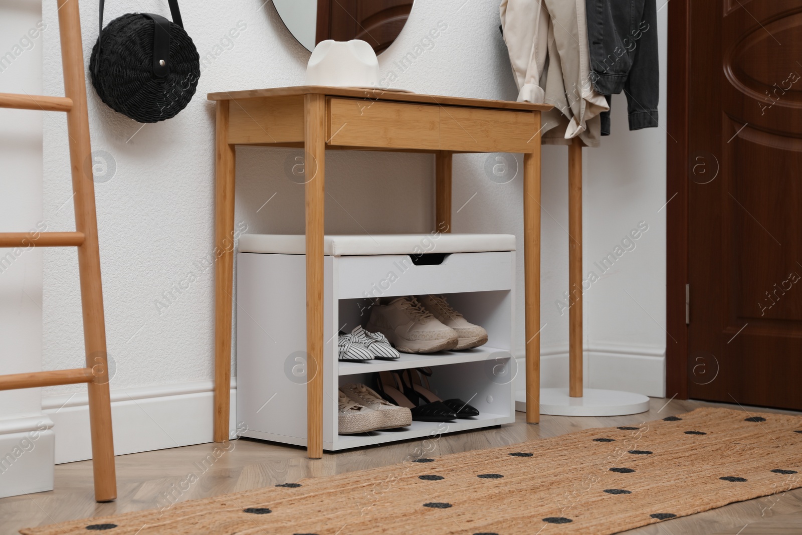 Photo of Shelving unit with shoes and accessories near white wall in hall