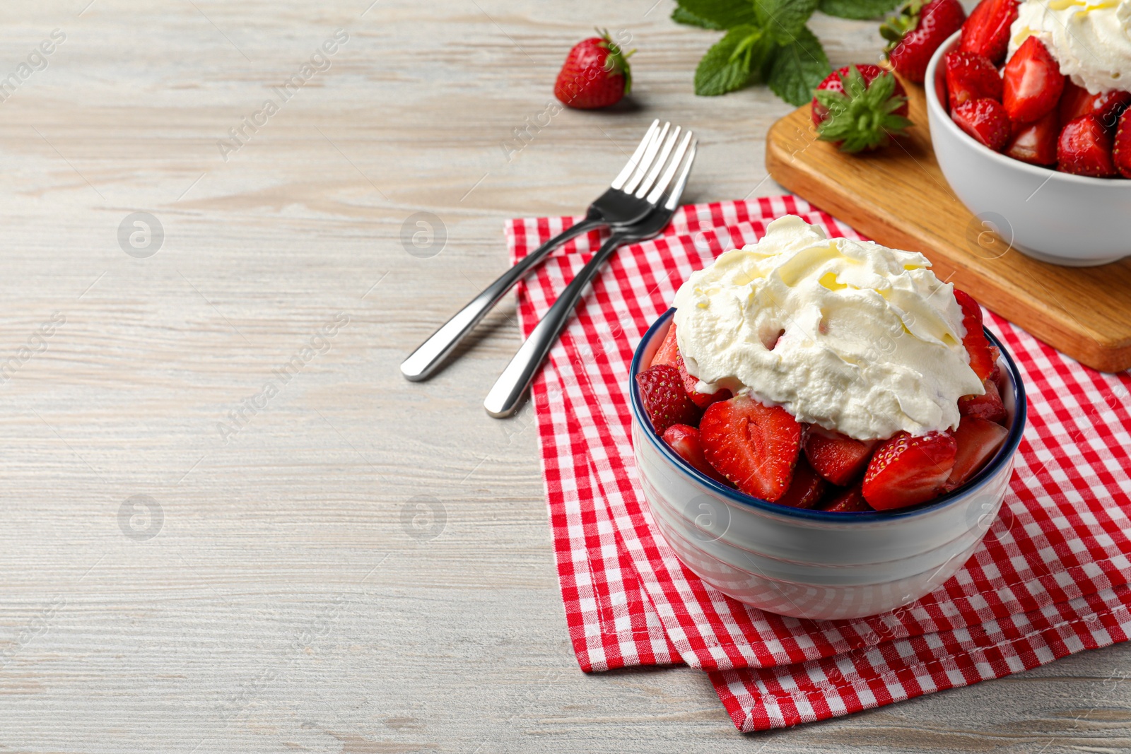 Photo of Delicious strawberries with whipped cream served on wooden table, space for text