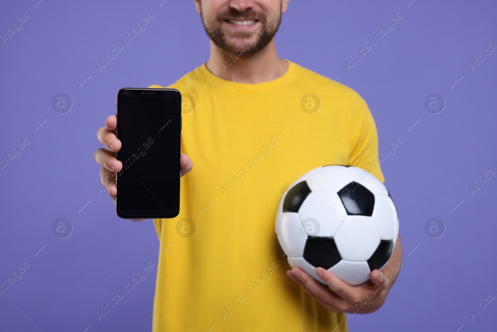 Photo of Sports fan with ball and smartphone on purple background, closeup