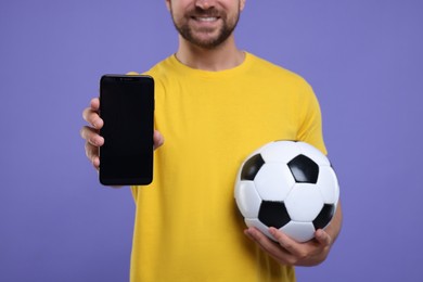 Sports fan with ball and smartphone on purple background, closeup