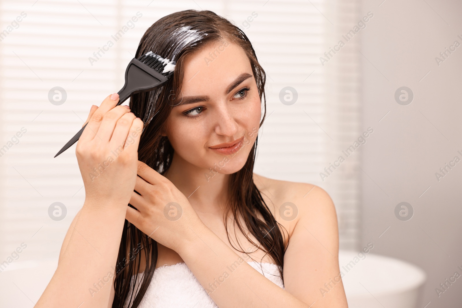 Photo of Young woman applying hair mask in bathroom