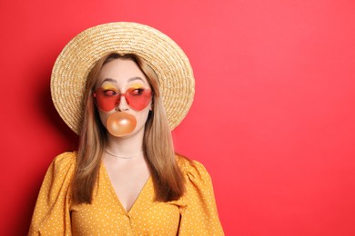 Photo of Fashionable young woman with bright makeup blowing bubblegum on red background, space for text