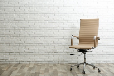 Comfortable office chair near white brick wall indoors. Space for text