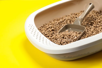 Photo of Cat litter tray with filler and scoop on yellow background, closeup