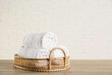 Wicker basket with rolled bath towels on wooden table near white brick wall. Space for text