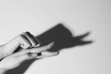 Photo of Shadow puppet. Woman making hand gesture like snail on light background, closeup. Black and white effect