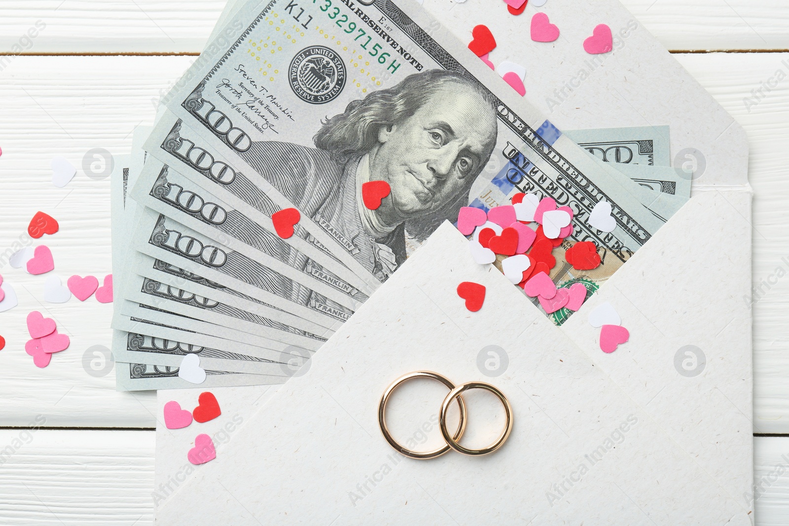 Photo of Honeymoon concept. Two golden rings, money and cutout hearts on white wooden table, flat lay