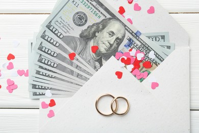 Honeymoon concept. Two golden rings, money and cutout hearts on white wooden table, flat lay