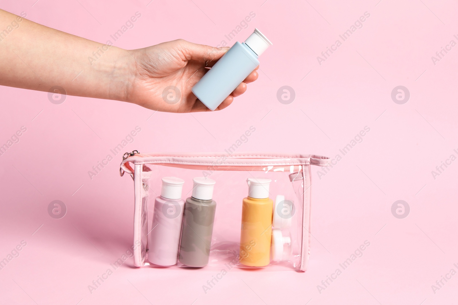 Photo of Cosmetic travel kit. Woman putting small bottle with personal care product into plastic bag against pink background, closeup