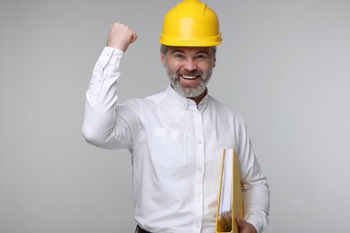 Architect in hard hat holding folder on grey background