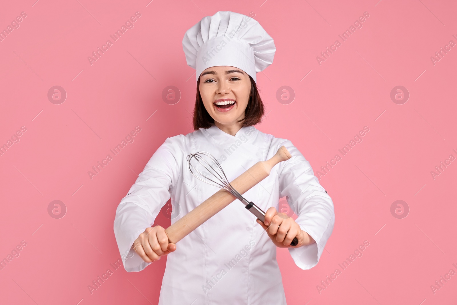 Photo of Happy confectioner with rolling pin and whisk on pink background