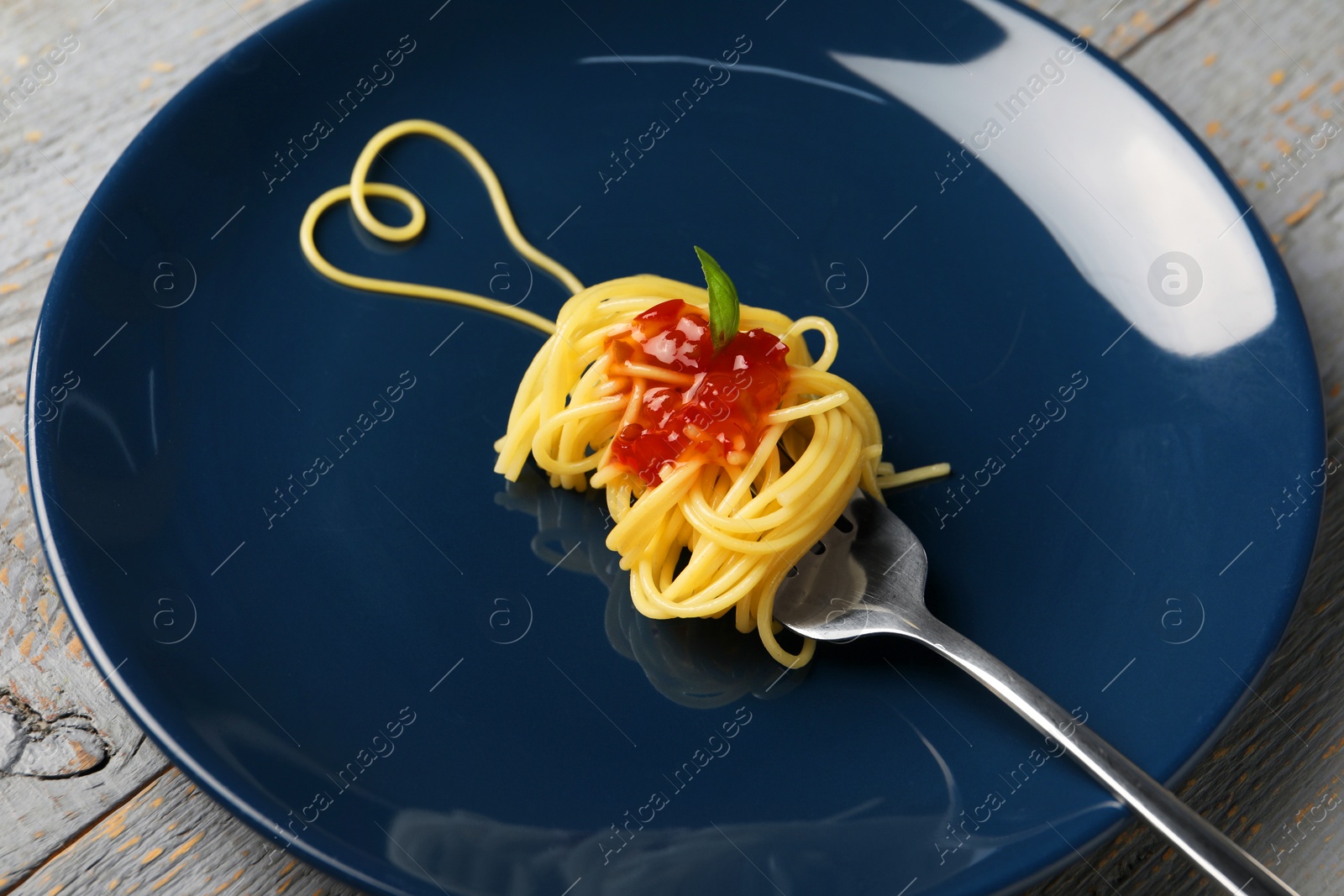 Photo of Heart made with spaghetti and fork on grey wooden table, closeup