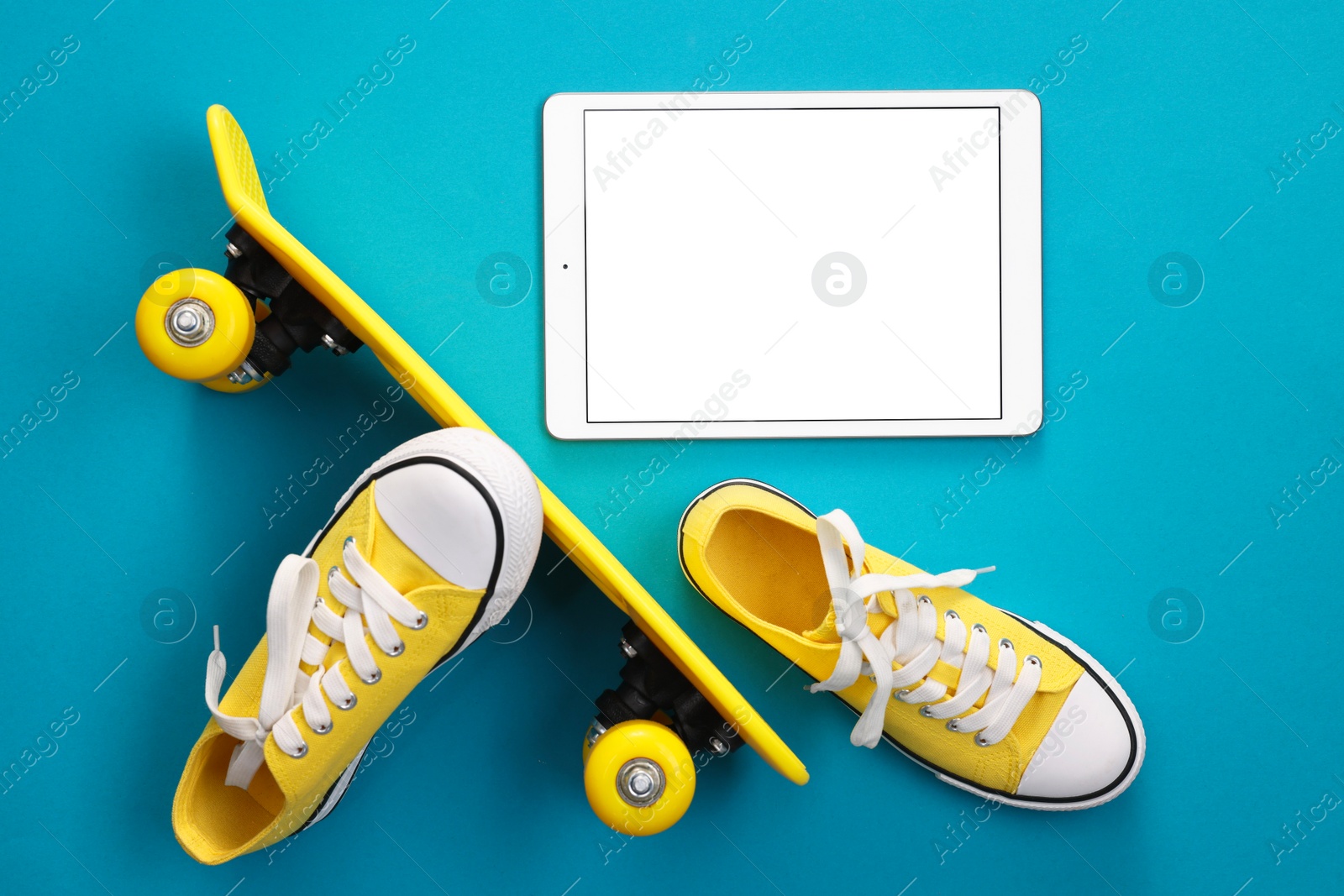 Photo of Modern tablet, skateboard and shoes on light blue background, flat lay. Space for text