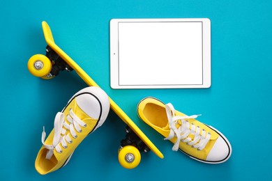 Modern tablet, skateboard and shoes on light blue background, flat lay. Space for text