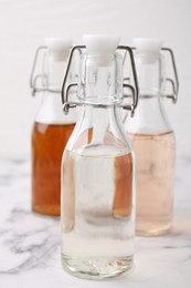 Different types of vinegar in bottles on light marble table, closeup