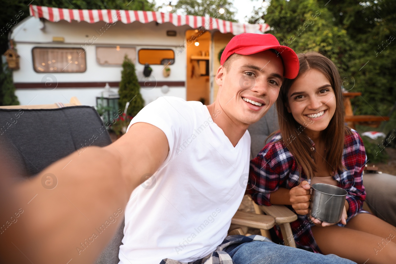 Photo of Happy couple taking selfie near trailer. Camping season