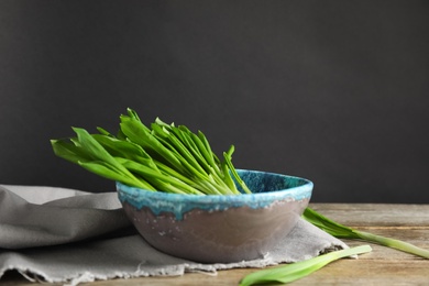 Bowl with wild garlic or ramson on wooden table against black background. Space for text