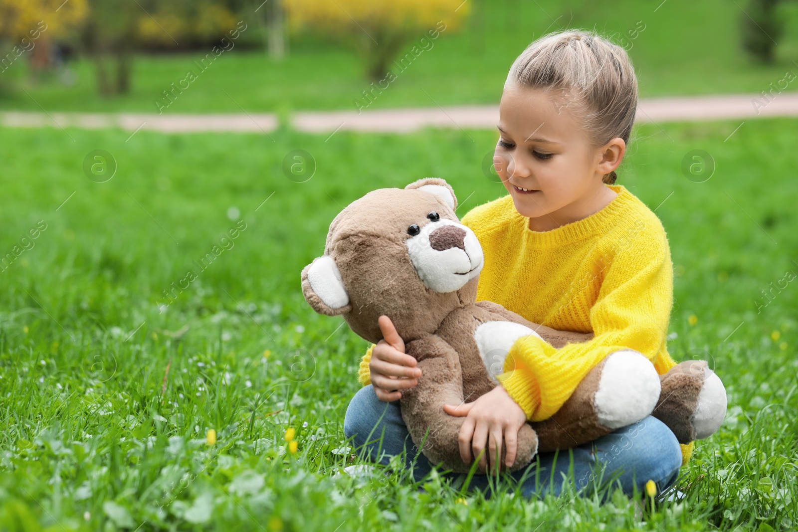 Photo of Little girl with teddy bear on green grass outdoors. Space for text