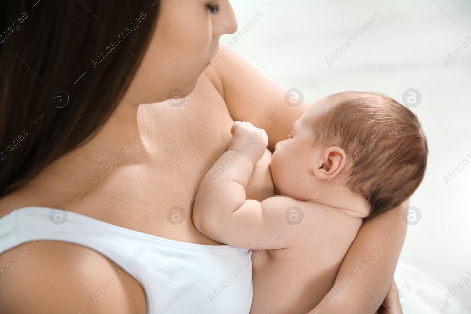 Photo of Young woman breastfeeding her baby on light background, closeup