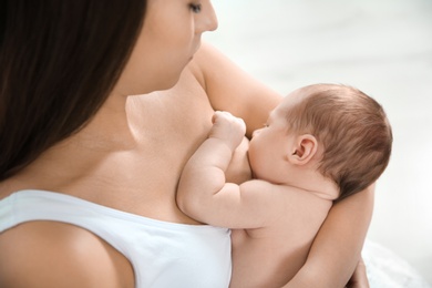 Young woman breastfeeding her baby on light background, closeup