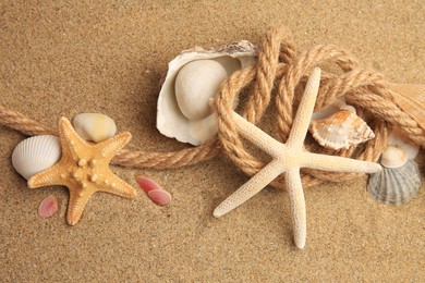 Photo of Beautiful sea stars, shells and rope on sand, above view