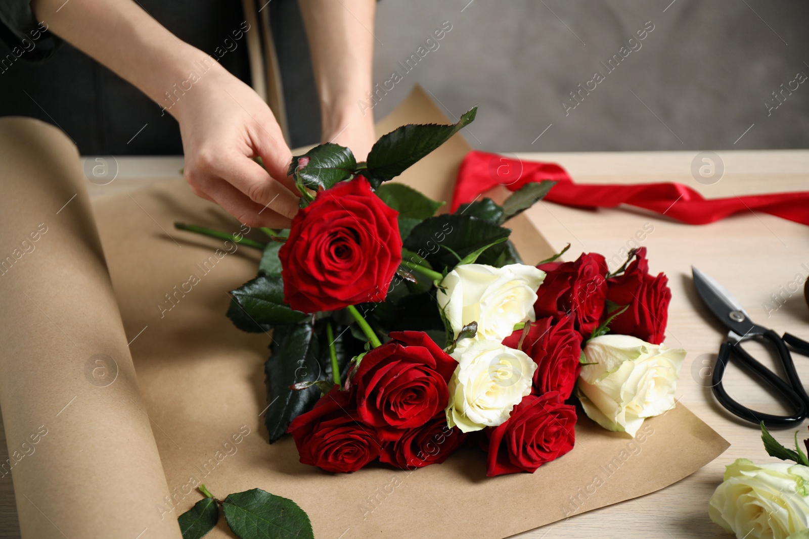 Photo of Woman making luxury bouquet of fresh roses at wooden table, closeup