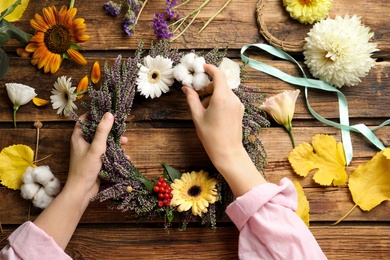 Florist making beautiful autumnal wreath with heather flowers at wooden table, top view