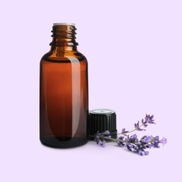 Bottle of lavender essential oil and flowers on pale light violet background