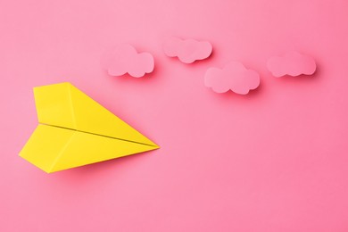 Photo of Handmade yellow paper plane with clouds on pink background, flat lay. Space for text
