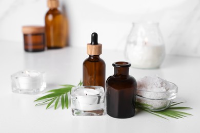 Photo of Essential oils, sea salt and candles on white table in bathroom, closeup