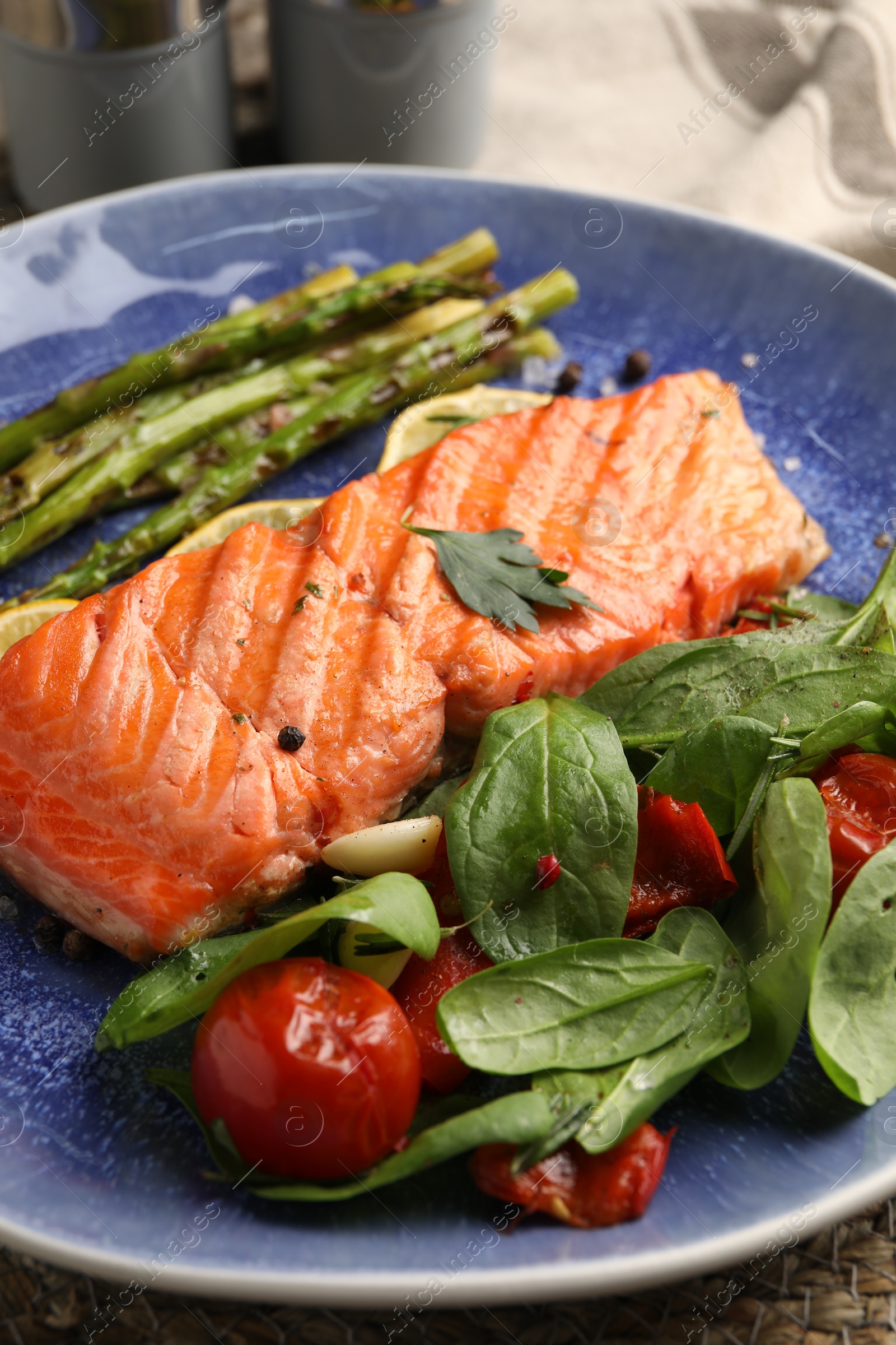 Photo of Tasty grilled salmon with tomatoes, asparagus, spinach and spices on table, closeup