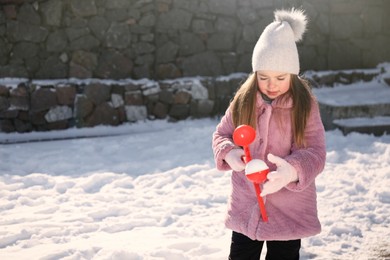 Photo of Cute little girl playing with snowball maker outdoors