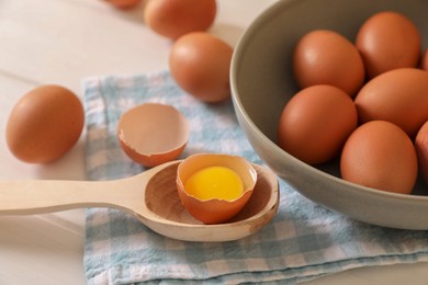 Fresh raw chicken eggs with bowl, spoon and napkin on white wooden table, closeup
