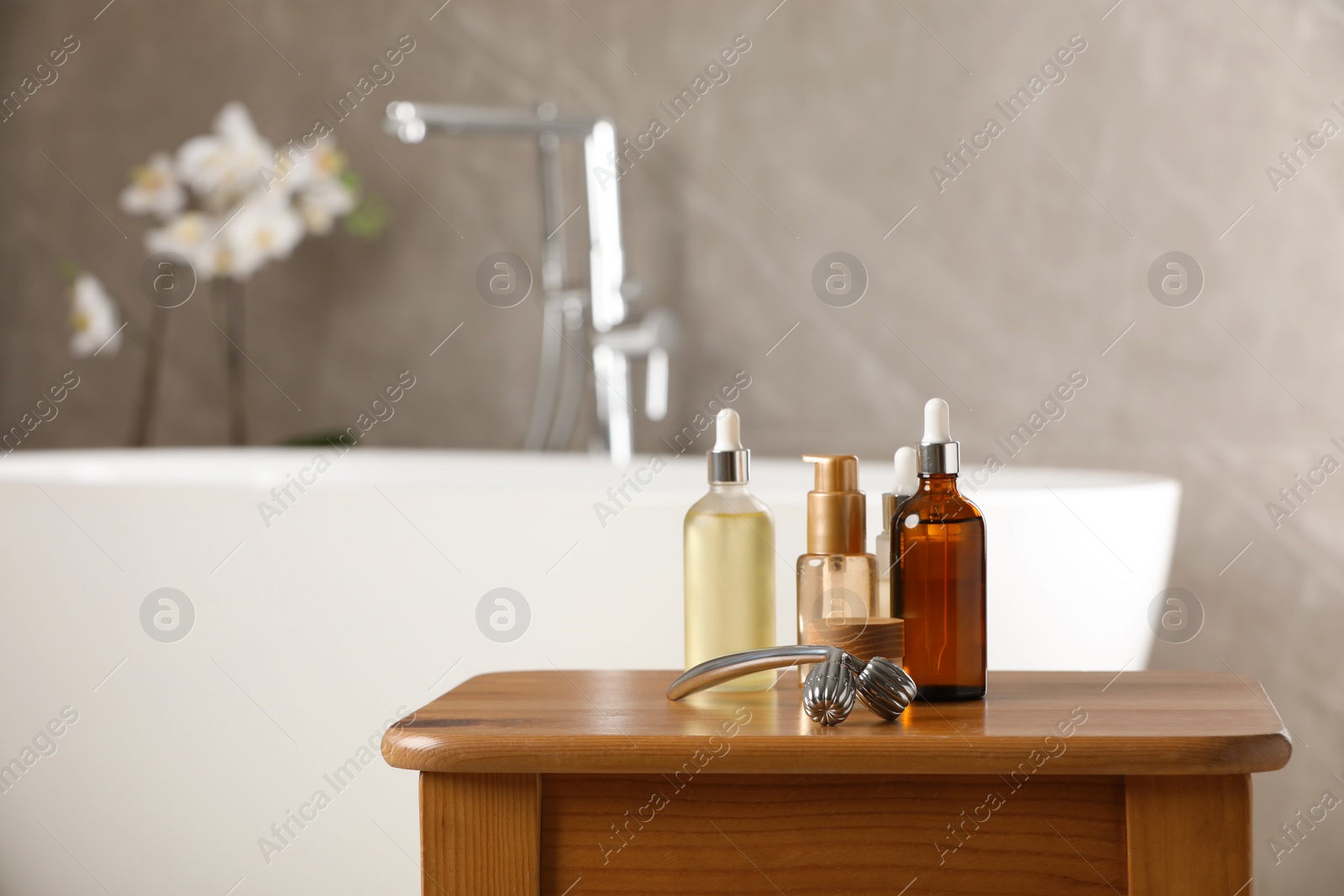 Photo of Metal face roller and cosmetic products on wooden table in bathroom. Space for text