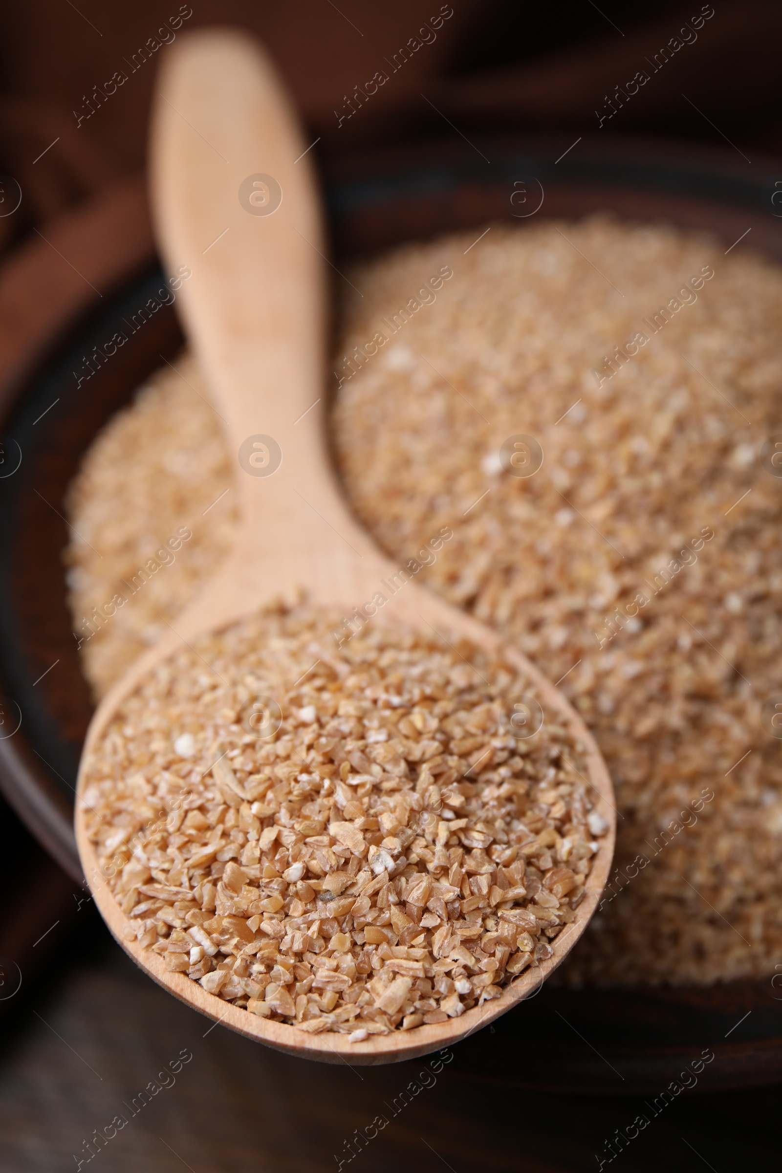Photo of Dry wheat groats in bowl and spoon on table, closeup