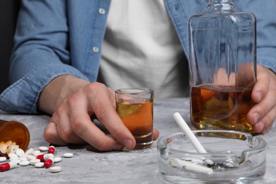 Photo of Alcohol and drug addiction. Man with whiskey, pills and smoldering cigarettes at grey textured table, closeup