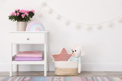 Stand with houseplant and toys near light wall in baby room. Interior design