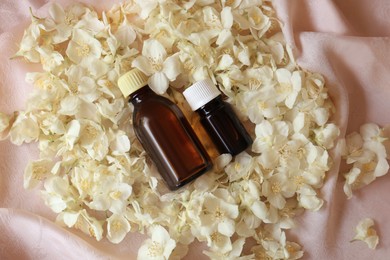 Bottles of jasmine essential oil and white flowers on pink fabric, flat lay