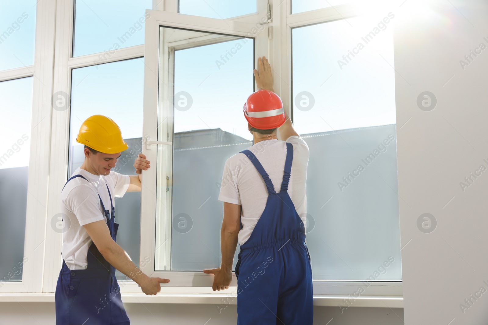 Photo of Workers in uniform installing plastic window indoors