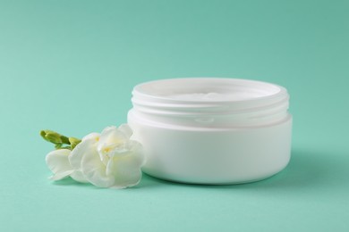 Moisturizing cream in open jar and freesia flower on turquoise background. Body care product